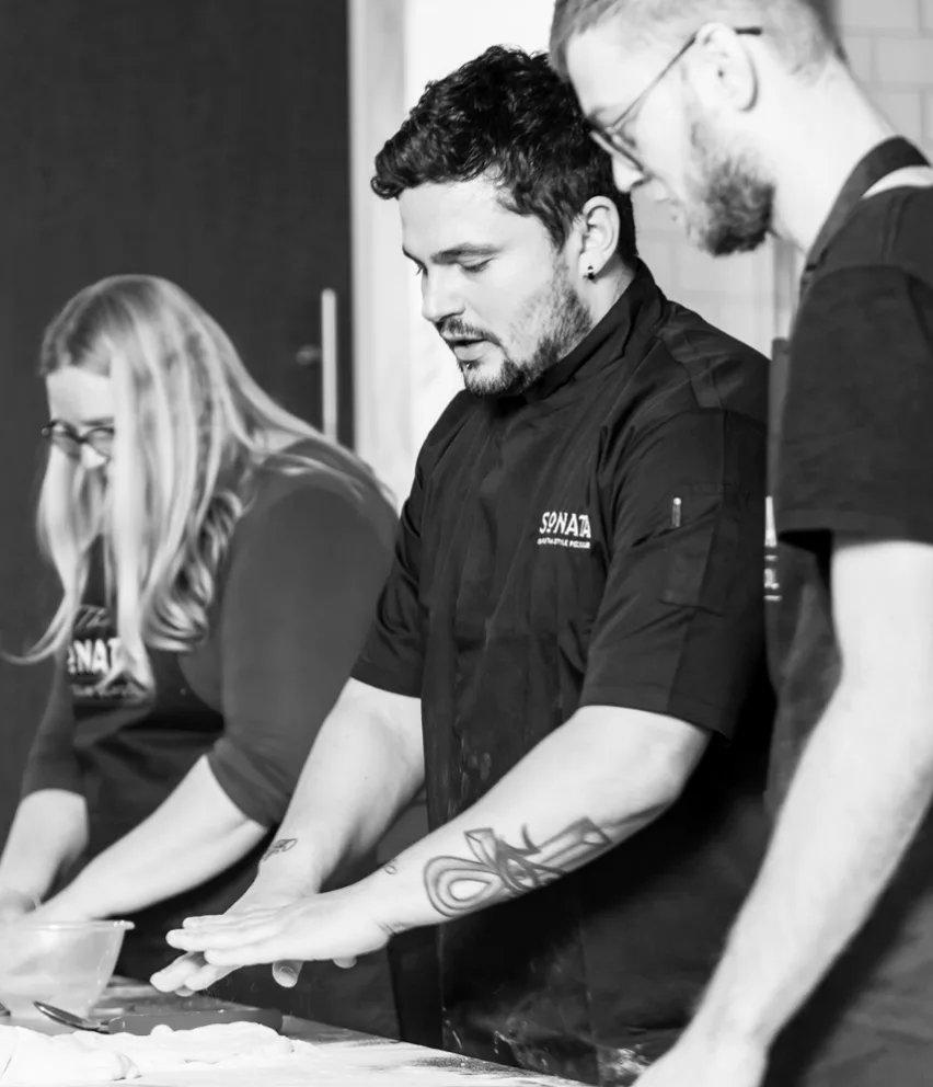 Chef showing attendee how to make pizza dough at sonata pizza school. Image is in black and white.